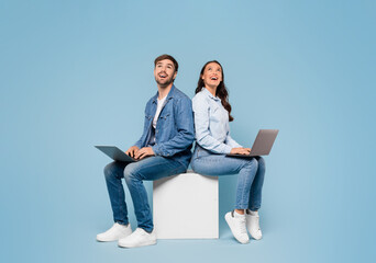 Couple with laptops look at free space on blue background - Powered by Adobe