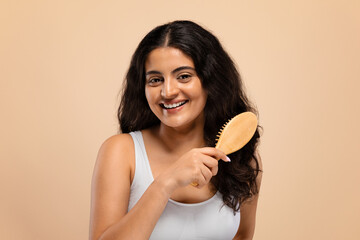 Smiling beautiful indian woman brushing her thick curly hair with bamboo comb