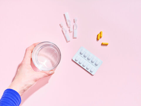 Flat lay creative composition with food supplement pills, glass of water and female hand on colorful background