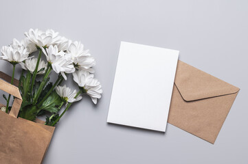 Craft envelope, blank mold and bouquet of white chrysanthemums in a craft gift bag on a gray...