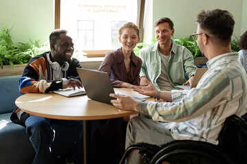 Young businessman with disability showing presentation on laptop to his colleagues