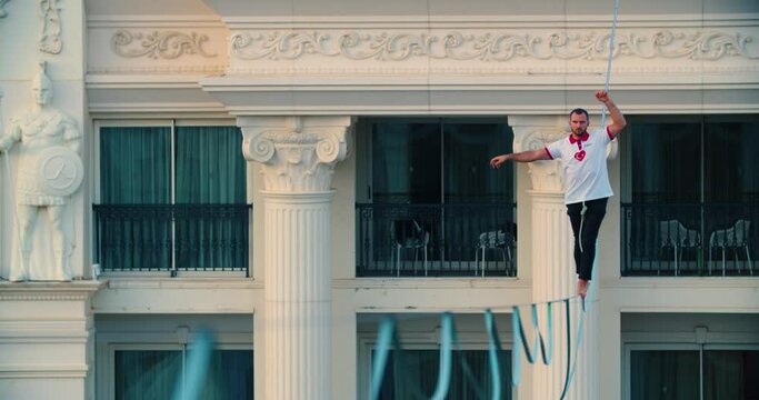 Slackline, man with amazing balance is walking the rope between two buildings 4k