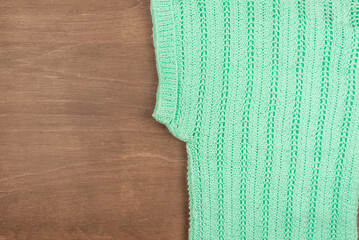 Top view of knitted green wool sweater on wooden background