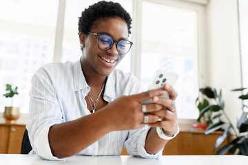 Charming charismatic african-american young businesswoman scrolling news feed on the smartphone,...