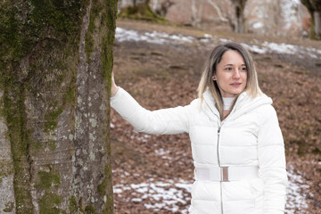 a woman in a white coat touching a tree trunk in a snowy forest