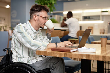 Young businessman with disability drinking coffee while working online in cafe