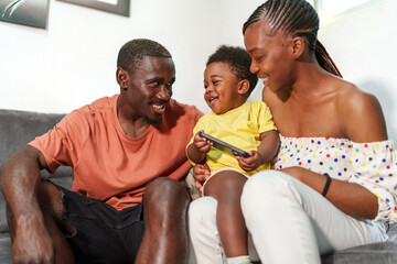 Cheerful African family with a child engaged with a smartphone, sharing a joyful moment at home.
