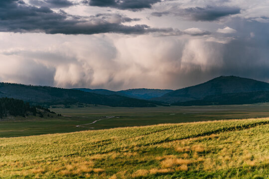 Thunderclouds roll over a meadow and mountains in the Valles Caldera National Preserve, New Mexico