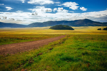 A dirt road leads through a meadow and mountains in the Valles Caldera National Preserve, New Mexico