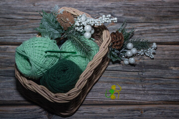 green yarn in basket and on wooden textured background and  knitting markers, decorative christmas branch, crochet hook.