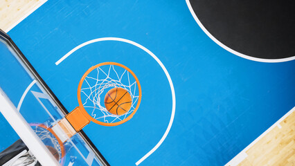 Top Down Shot Of Basketball Ball Going Through a Hoop At Sports Court In International Arena. Empty Playing Field Where Professional Matches And Games Are Held Awaiting For Begining Of Tournament.