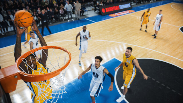 Cinematic College Basketball Tournament: Two Young Successful Diverse Teams Play a Championship Match in Modern Arena. Excited African Player Scores a Perfect Slam Dunk with Two Hands.