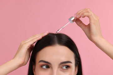 Woman applying hair serum on pink background, closeup. Cosmetic product
