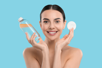 Beautiful woman holding makeup remover and cotton pad on light blue background