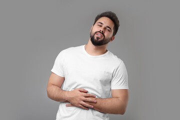 Young man suffering from stomach pain on light grey background - obrazy, fototapety, plakaty