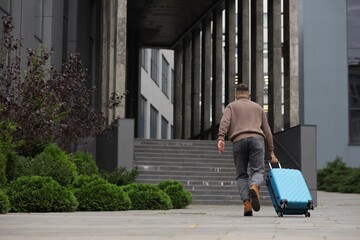 Being late. Man with suitcase running towards building outdoors, space for text