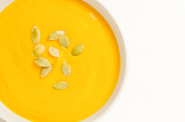 Pumpkin cream soup with dried seeds in a gray bowl on a white tablecloth. Concept of healthy eating. Vegetarian and vegan food. Horizontal orientation. Copy space. Top view