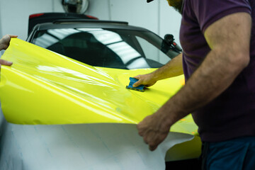 Car Detailing and Wrapping Workshop, Working on a Black and Yellow Car. Car Wrapping Process: Applying Adhesive Vinyl to the Vehicle