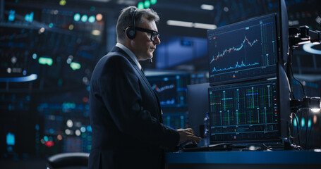 Stylish Adult Stock Exchange Broker Working on a Desktop Computer with Real-Time Stocks,...