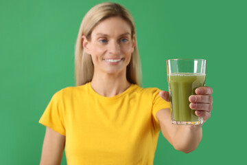 Woman with glass of tasty celery juice on green background, selective focus