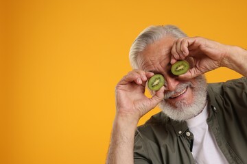 Senior man covering eyes with halves of kiwi on orange background, space for text