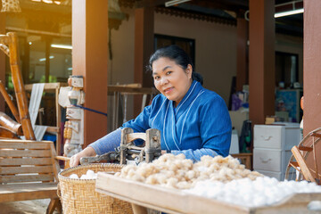 Asian female tourist spins cotton to remove the seeds in a manual cotton gin. at the demonstration...