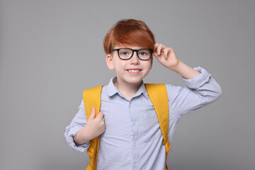 Happy schoolboy with backpack on grey background