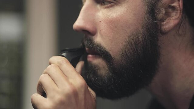 Cinematic shot of brutal bearded man shaves his beard, morning tradition, self-care. Barbershop and cosmetology. Close-up portrait, facial features and handsome man