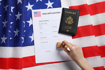 Immigration to USA. Woman stamping visa application form on flag, top view