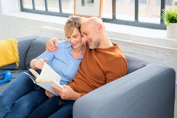 Shot of a married couple reading a book together and relaxing on the sofa at home