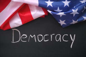 The flag of the USA lying on a chalkboard with the word Democracy written on it. Close up.
