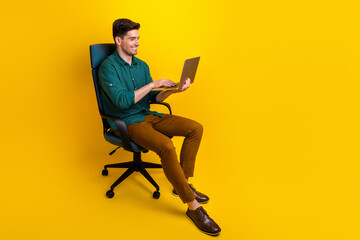 Photo of nice successful man wearing stylish clothes sitting armchair writing sms message empty space isolated on yellow color background