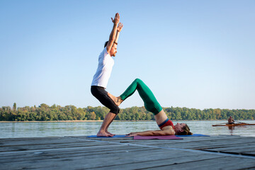 Fototapeta na wymiar Couple practicing yoga on wooden deck by the river