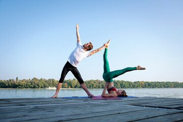 Couple practicing yoga on wooden deck by the river