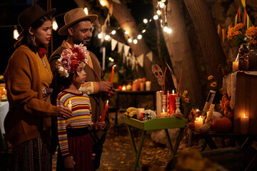 Family of three standing in front of altar with candles and celebrating the mexican holiday