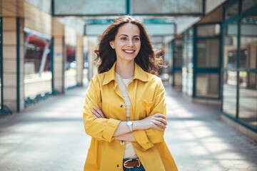 Candid portrait of a cheerful young woman wearing an yellow shirt spending time in the city. The pretty female has a joyful expression. Successful proud woman in city street at sunset