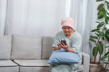 Fototapeta premium Asian female patient with cancer, but recovering at home, sitting using phone on phone inside house, my mother's expression was not strong, because had just recently had surgery.