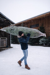 Handsome bearded man holding wrapped Christmas tree on fair. Happy male bring fir tree.