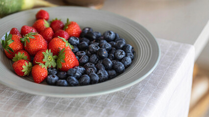 Fresh strawberries and blueberries on a white plate on kitchens table, close-up, selective focus.