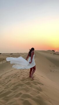 beautiful girl in a white dress in the sandy desert against the backdrop of sunset