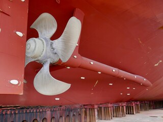 ship in dry-dock, bronze propeller and rudder on red hull	
