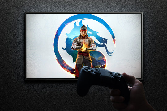 Mortal Kombat 1 game on TV screen with gamepad in hand on black textured wall with light.