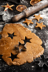 Close-up of gingerbread cookie dough with stars on wooden table with flour, rolling pin and oranges, vertical