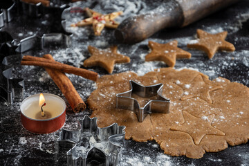Close-up of gingerbread cookie dough with stars on wooden table with candle, flour and rolling pin, horizontal