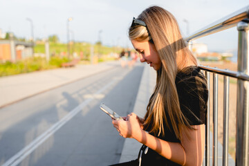 A teenage girl holds a smartphone in her hands and chats on the city embankment in summer