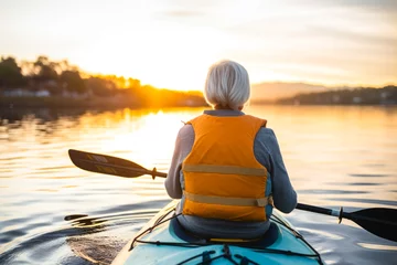 Foto op Canvas Rear view of a retired older woman enjoying a peaceful moment while canoeing or kayaking on calm waters during late afternoon. A serene scene, contemplative solitude and tranquility © MVProductions
