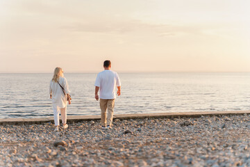 A charming couple in a white shirt walks along the shore at sunset in summer,rear view. Togliatti,...