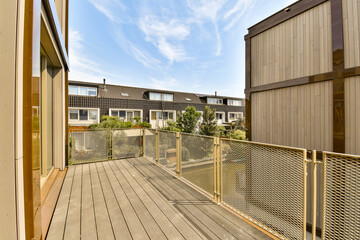 an outside area with wooden decking and metal railing on the right side of the photo, there is a building in the background - Powered by Adobe
