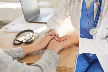 Close up photo of young female physician holding hands her patient in palms. Woman doctor in white coat supporting her sick patient in hospital or clinic office after test results at checkup. - Powered by Adobe