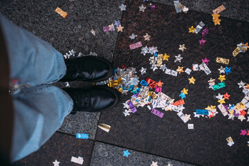 Women's feet in black boots on the asphalt with Christmas confetti from a firecracker. Confetti...